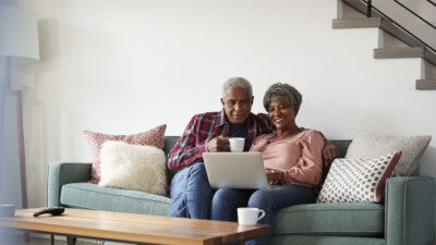 A man and a woman sitting on the couch, looking at a laptop.