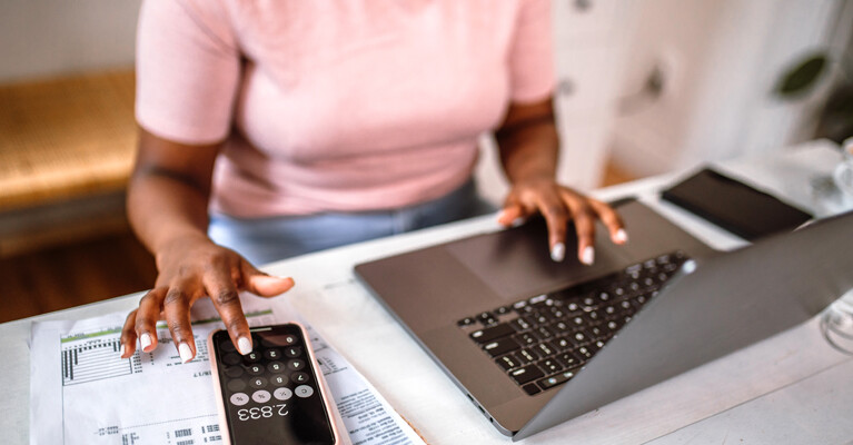 A woman using a laptop and her phone.