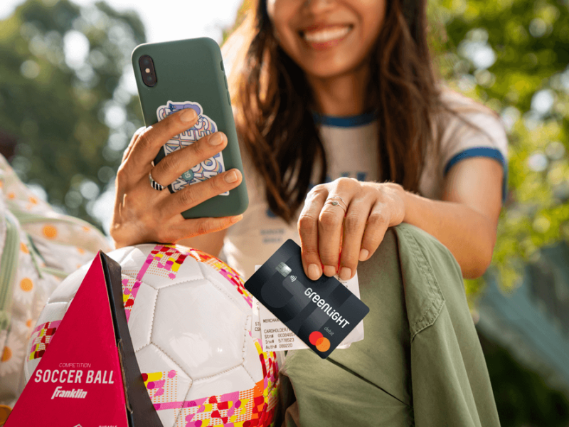 Woman holding a debit card in her hand at a soccer field.